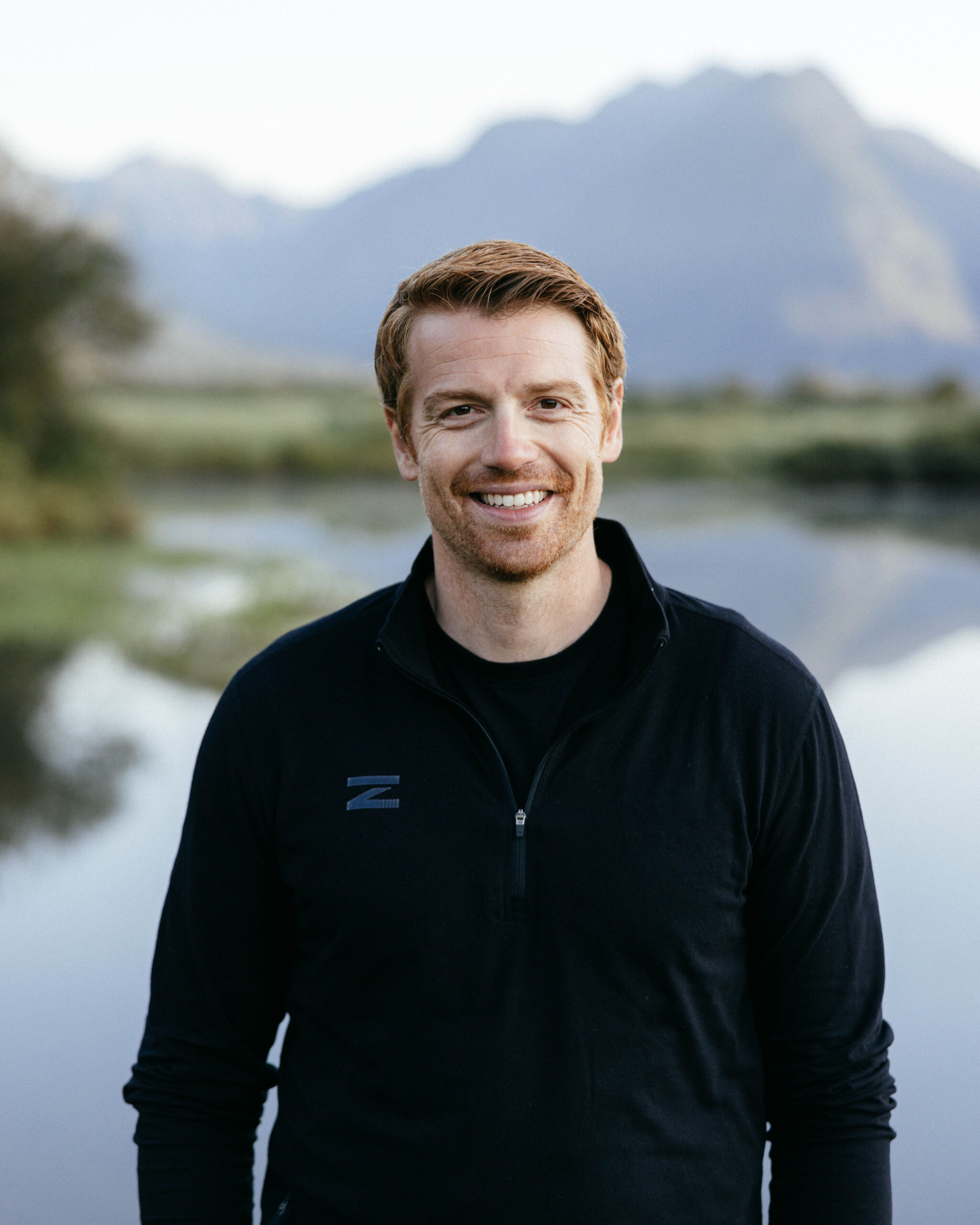 Douglas Lynch wearing a black Zenkai Hoodie with a lake in the background